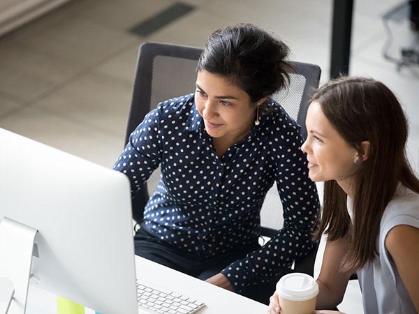 2 woman sitting in office chairs looking at a monitor