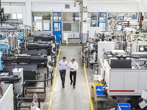 photo of two men talking while walking through an industrial production room
