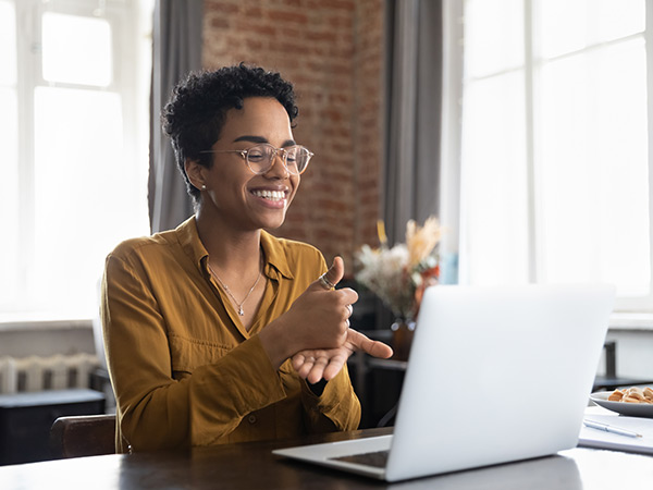 Smiling friendly African American therapist in glasses talking on video call, using sign language, speaking to patient with hearing disability, deafness, showing gestures at screen