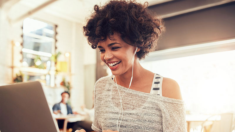 Woman wearing ear buds and smiling at her laptop screen