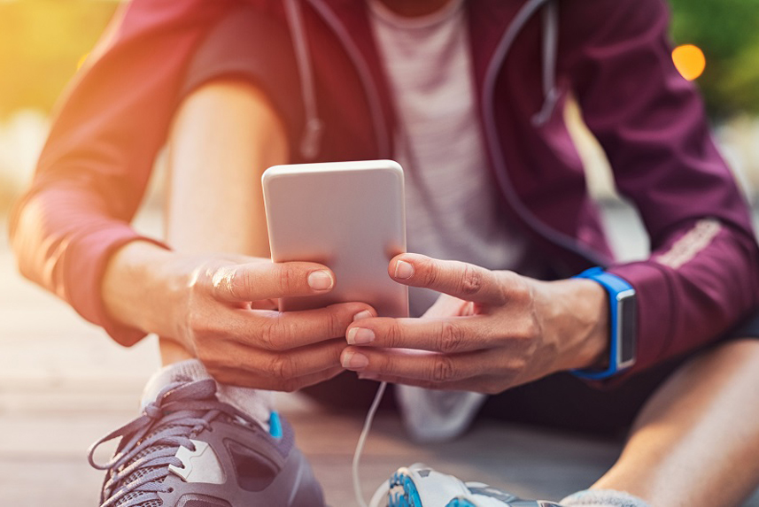 Person dressed for exercise, sitting on the ground checking fitness app on smartphone