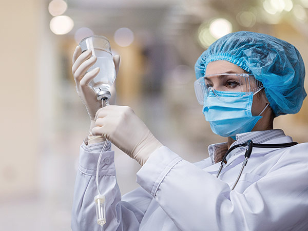 Medical staff member in full protective gear connecting an IV line to a bottle of clear liquid