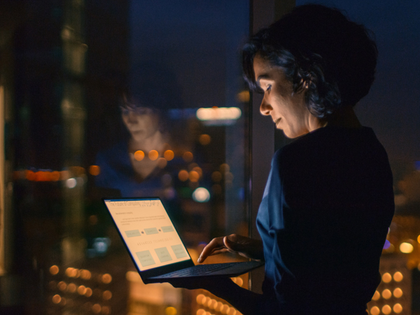 woman looking at a laptop with city skyline at night in the background