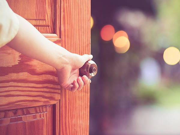 Hand grasping a door knob and opening a door.