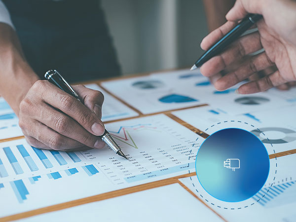 Two people reviewing printed charts and graphs with pens, analyzing financial or business data.
