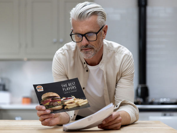 man leans on a kitchen counter while looking at a save mailer