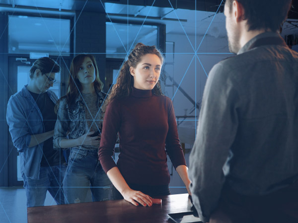 woman standing infront of a desk with a semitransparent blue digital wall behind her