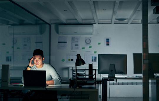 man sitting in a dark office space using a laptop