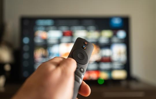 A person holds a remote in front of a vibrant TV screen, ready to browse and enjoy shows