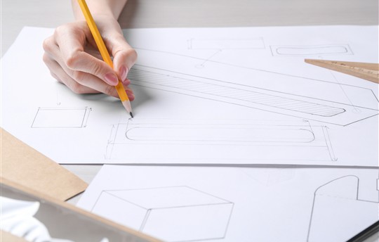 Woman creating packaging design at light wooden table, closeup 