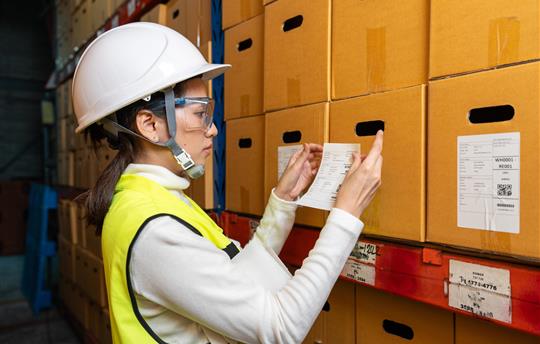 woman puts a barcode sticker on a cardboard box in a warehouse.