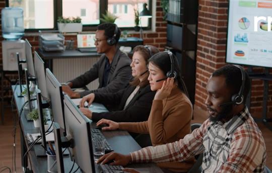 Four call center employees sitting at a table wearing headsets