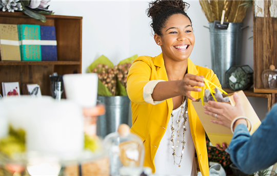 Smiling woman clerk handing a shopping bag to a customer