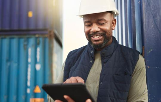 Man wearing a hard hat near freight containers using a tablet