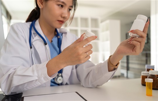 Female doctor writing in a notebook and holding a medicine bottle 